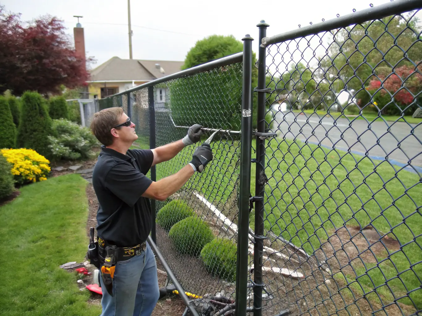 A handyman repairing a wooden fence in a residential backyard, highlighting the importance of timely repairs to prevent further damage.